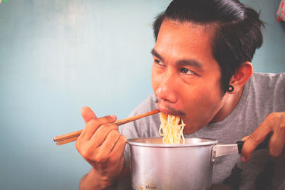 Close-up of man eating noodles against wall