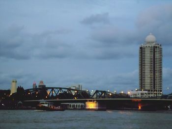 Illuminated bridge over river by buildings against sky