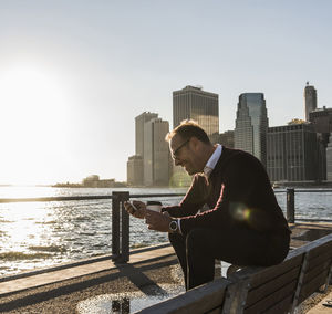 Usa, brooklyn, smiling man with coffee to go sitting on bench looking at smartphone