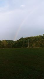 Scenic view of rainbow over trees on field against sky