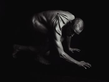 Side view of depressed naked man with tattoo bending against black background