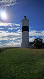 Lighthouse on field against cloudy sky