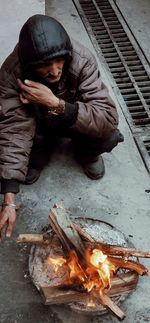 High angle view of man crouching by fire pit during winter