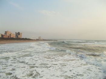 Calm sea with buildings in background against clear sky