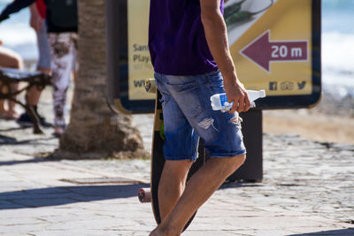 Midsection of man with bottle walking on footpath