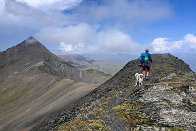 Rear view of man and dog walking on mountain against sky