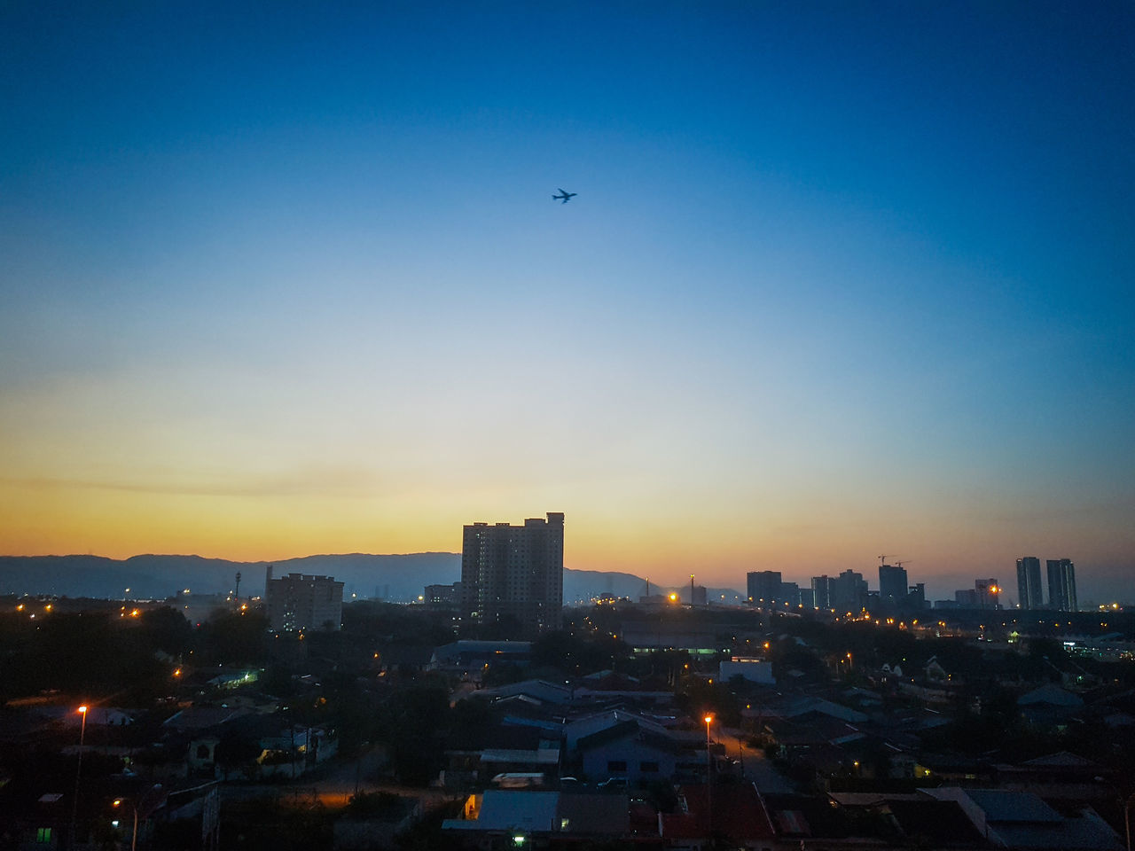AIRPLANE FLYING OVER BUILDINGS AGAINST SKY DURING SUNSET