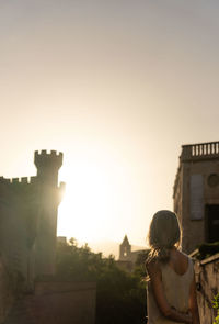 Rear view of woman standing against clear sky during sunset