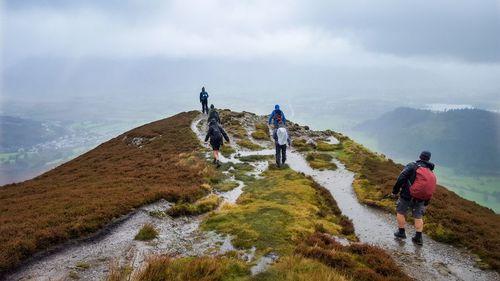 Rear view of people walking on mountain against cloudy sky