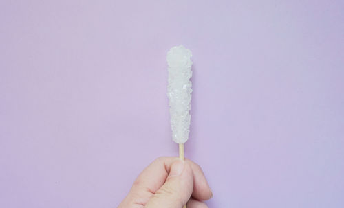 Close-up of hand holding ice cream against white background