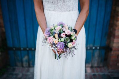 Close-up of woman holding bouquet against blue wall