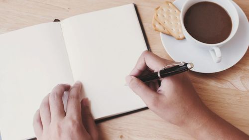 Cropped hands writing by coffee cup on table