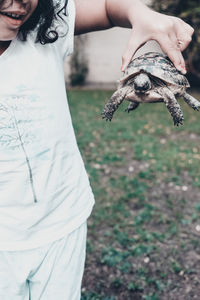 Midsection of girl holding turtle in yard