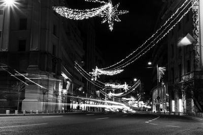 Illuminated light trails on street amidst buildings in city at night