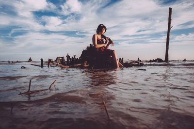 Young woman sitting in sea against cloudy sky