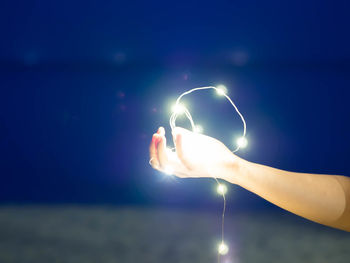 Cropped hand of person holding illuminated string lights at night