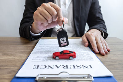 Midsection of man holding car key over papers and toy on table