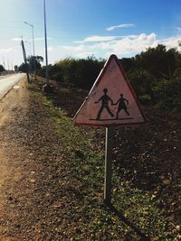 Road sign by trees against sky