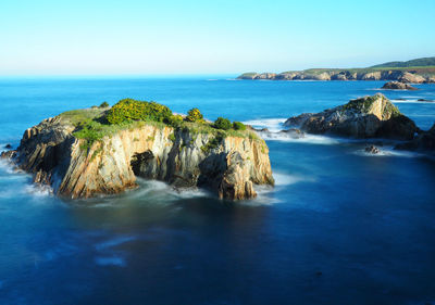 Rock formation in sea against clear blue sky