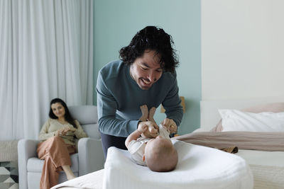 Happy father changing clothes of baby boy in bedroom at home