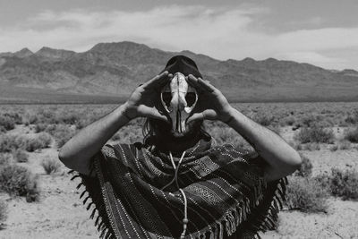 Man holding mask while standing on land against sky