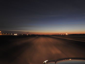 Illuminated road against sky seen through car windshield