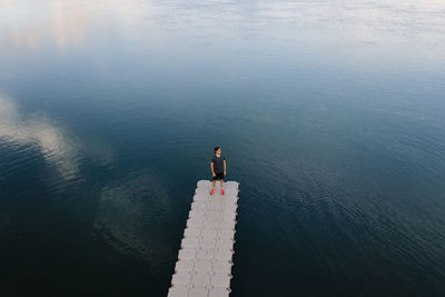 From above remote view of male standing on edge of quay near calm lake