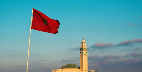 View of the famous hassan ii mosque and a waving moroccan flag against sky - casablanca,  morocco