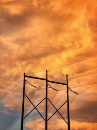 Low angle view of silhouette electricity pylon against dramatic sky