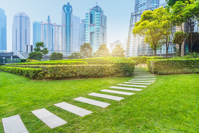 Park by buildings in city against sky