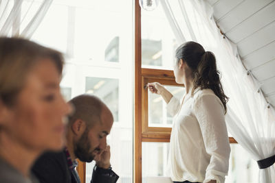 Mid adult businesswoman closing office window while colleagues in foreground