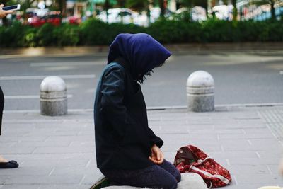 Person kneeling on sidewalk