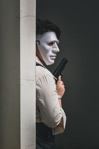 Portrait of a person wearing a mask holding up a fake gun behind a wall