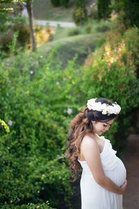 Side view of pregnant woman in dress wearing flower tiara by plants