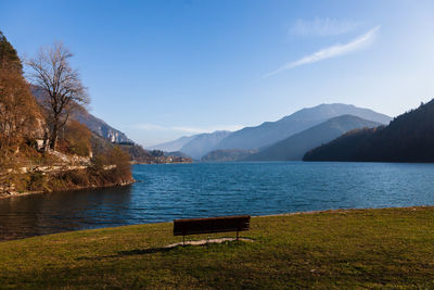 Bench by lake against sky