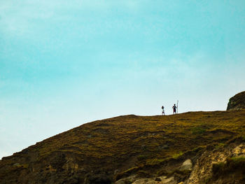 Low angle view of people standing on mountain against sky