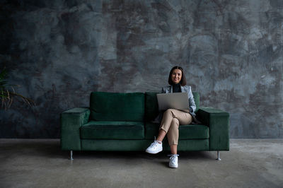 Young woman using laptop while sitting on sofa at home