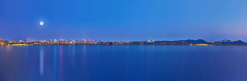 Illuminated city by sea against sky at night