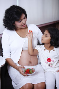 Cute girl feeding strawberry to pregnant mother at home