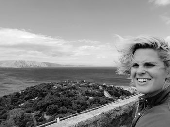 Portrait of smiling young woman on shore against sky