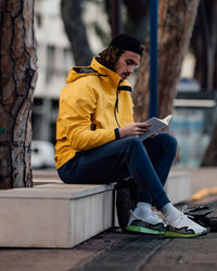 Full length of man reading book while sitting by tree