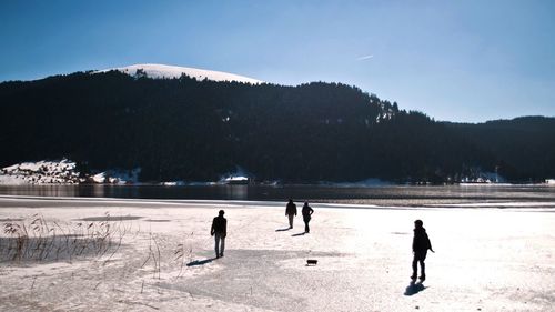 People walking at beach against mountains during winter