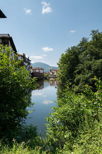 Scenic view of lake by trees and building against sky