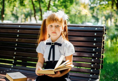 A child is sitting on a bench outside on a warm sunny day, and is returning to school. 