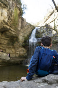 Back view of two young teenagers sitting on rock against waterfall