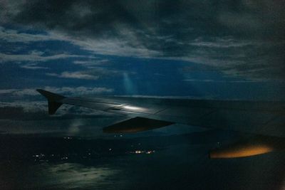 Cropped image airplane wing over sea against cloudy sky at night 