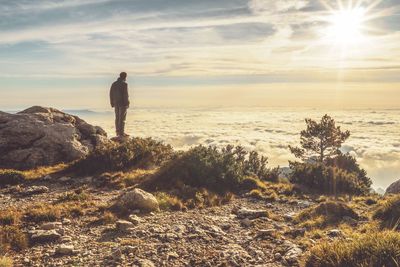 Rear view of man standing on rocky by cloudscape