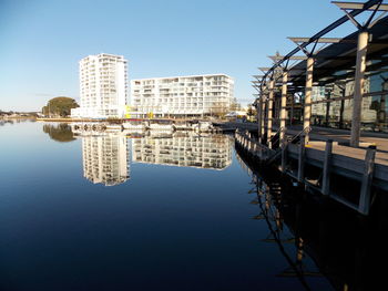 Reflection of buildings in city against clear sky