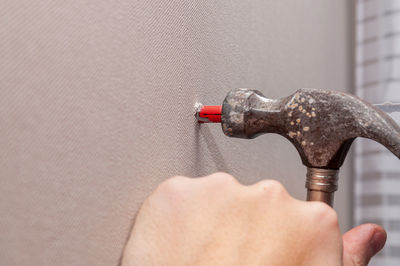 Close-up of hand holding faucet against wall