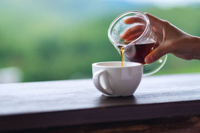 Closeup image of a hand pouring drip coffee into a white mug with blurred nature background